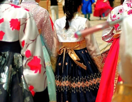 Women wearing colorful Korean traditional clothes including floral hanbok jeogori and embroidered navy chima skirts at a cultural ceremony