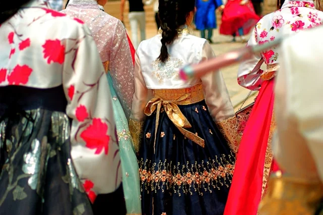 Women wearing colorful Korean traditional clothes including floral hanbok jeogori and embroidered navy chima skirts at a cultural ceremony