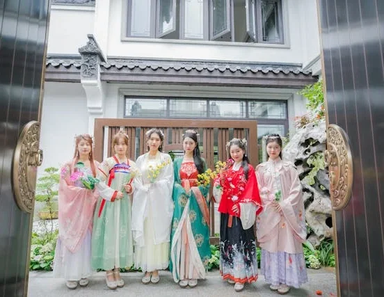 Group of women wearing traditional Chinese Hanfu dresses standing at the entrance of a traditional-style building with floral decorations.
