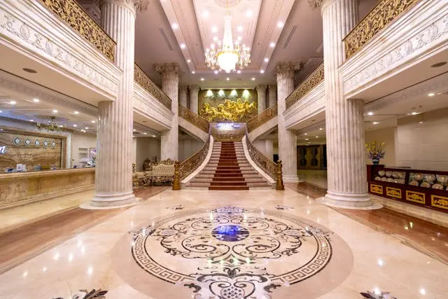 Luxury hotel lobby interior with grand staircase, marble columns, chandelier lighting, and elegant floor design